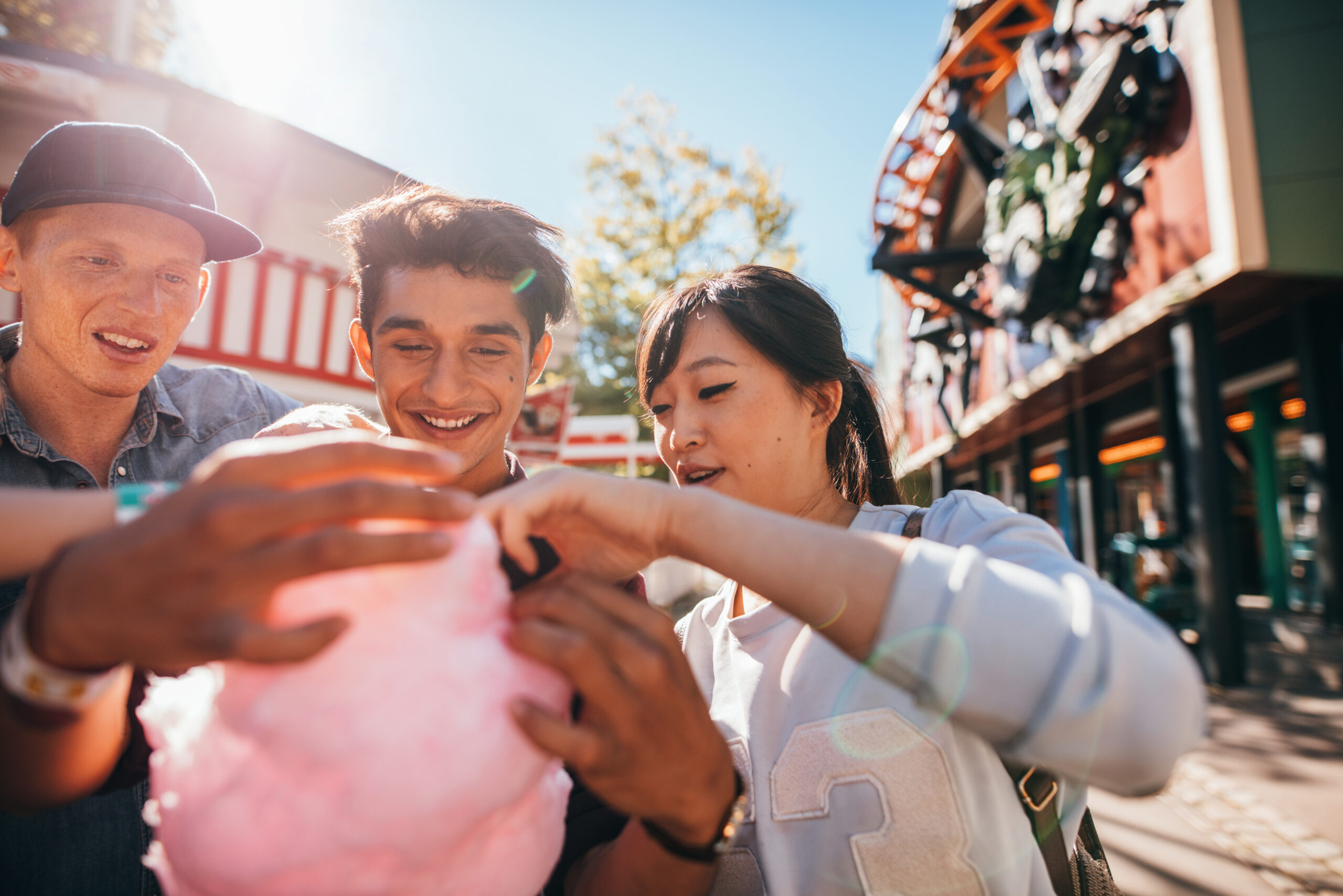 Young men and woman sharing cotton candy floss at fairground. Group of friends eating cotton candy in amusement park.